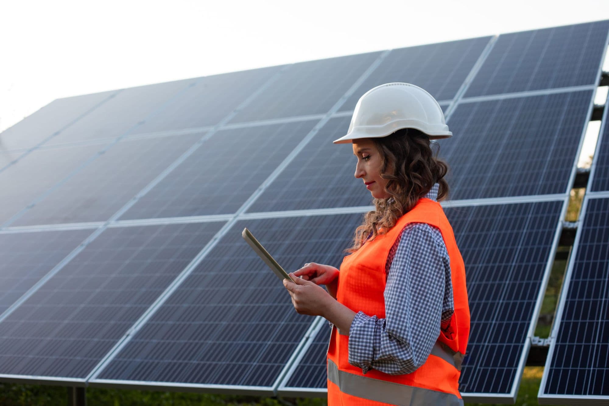 Technicienne casquée consultant une tablette devant une centrale solaire